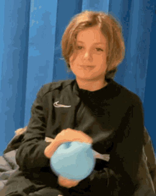 a boy wearing a black nike jacket holds a blue balloon