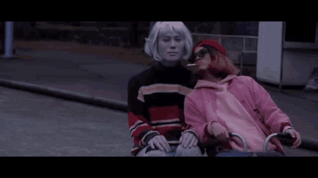 a woman in a pink jacket is sitting in a wheelchair next to a man with white hair