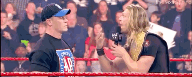 two wrestlers are talking to each other in a wrestling ring while a crowd watches .