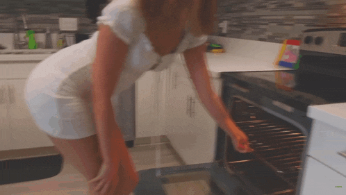 a woman in a white dress opens an oven door