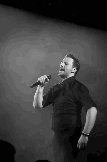 a man in a black shirt sings into a microphone in a black and white photo