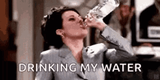 a woman is drinking water from a bottle while wearing a suit and tiara .