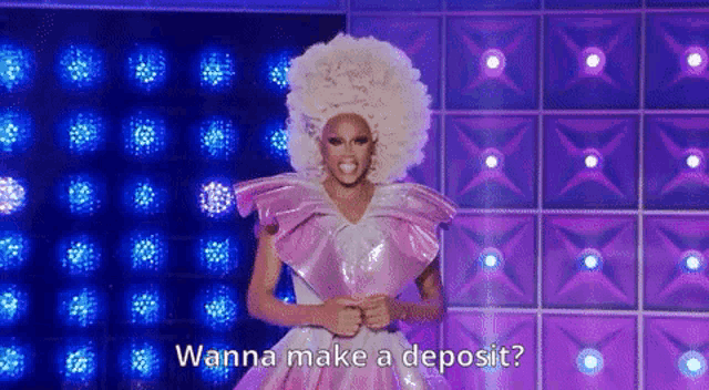 a drag queen is standing on a stage wearing a pink and white dress and a large afro wig .