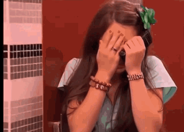 a young woman is covering her face with her hands while talking on a cell phone .