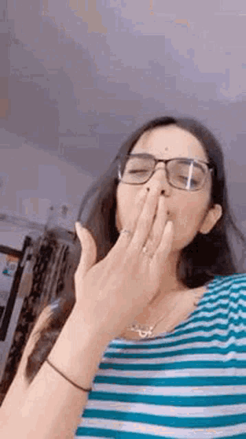 a woman wearing glasses is blowing a kiss with her hand .