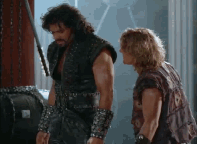 two men are standing next to each other in a room with a sword .