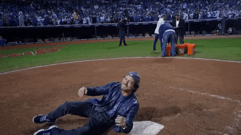 a man in a leather jacket is laying on the ground on a baseball field