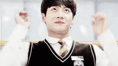 a young man in a school uniform and tie is making a heart shape with his hands .