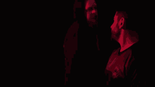 two men standing next to each other in a dark room