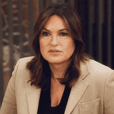 a close up of a woman wearing a tan jacket and black top