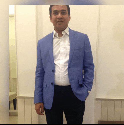 a man in a blue jacket and black pants stands in front of a white wall