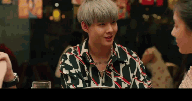 a man with a tattoo on his neck is talking to a woman in a restaurant