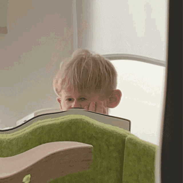 a young boy covering his face with his hand while looking at a book
