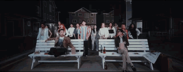 a group of people standing and sitting on white benches