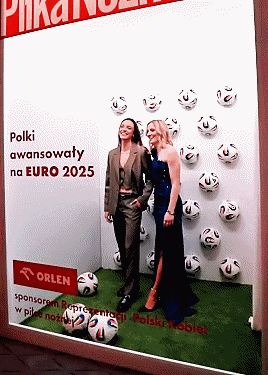 two women standing in front of a wall with soccer balls on it and a sign that says orlen