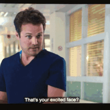 a man in a blue scrub top says that 's your excited face in a hospital hallway