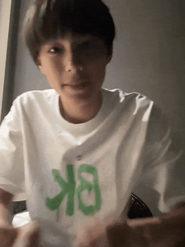 a young man wearing a white t-shirt with a green letter on it