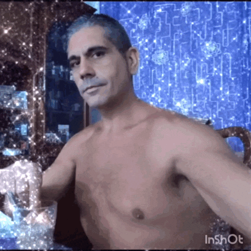a shirtless man is sitting at a table with a glass in his hand