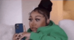 a woman in a green hoodie is sitting in a chair looking at her cell phone .