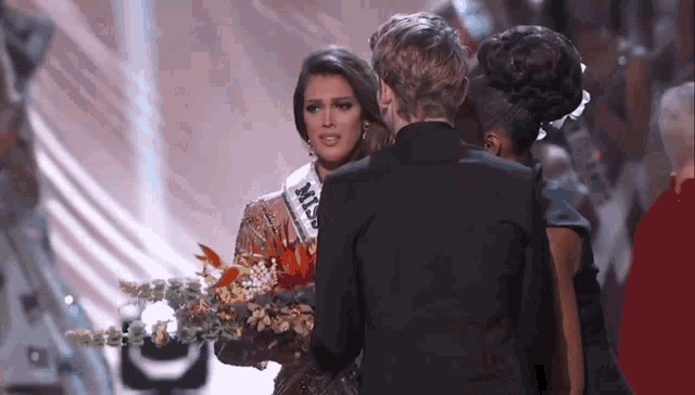 a woman wearing a miss universe sash is being congratulated by a man