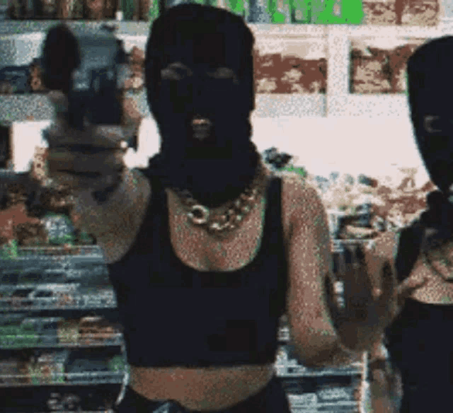 a woman wearing a ski mask is pointing a gun at another woman in a store .