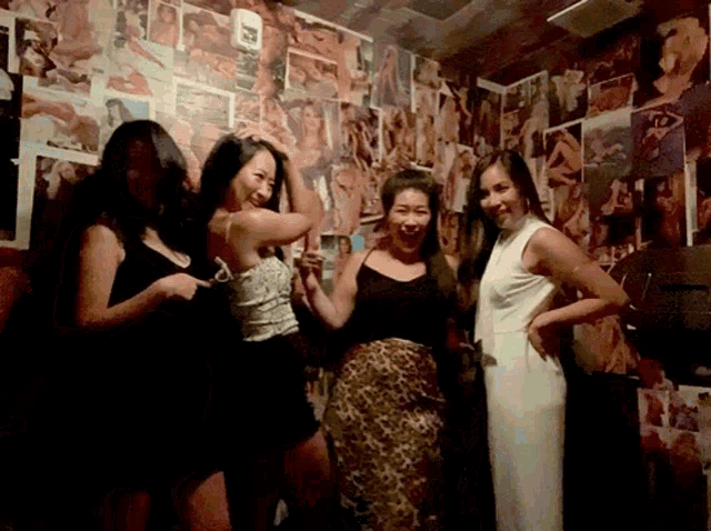 four women are posing for a picture in front of a wall with pictures of women