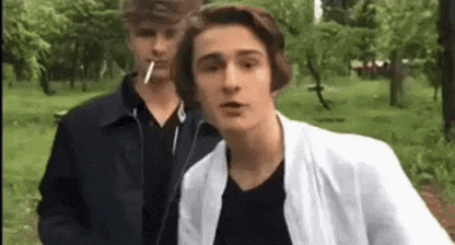 a man is smoking a cigarette while standing next to another man .
