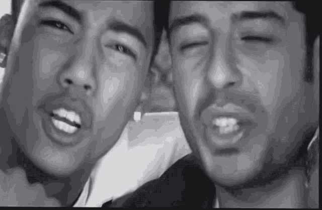a black and white photo of two men making funny faces with their eyes closed