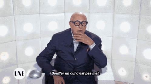 a man in a suit and glasses says bouffer un cul c'est pas mal while sitting in a chair