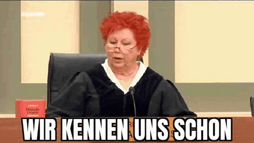 a judge with red hair is sitting at a table in front of a microphone and a book .