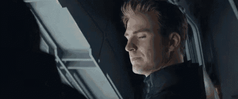 a man with long hair is sitting in a dark room looking out a window .