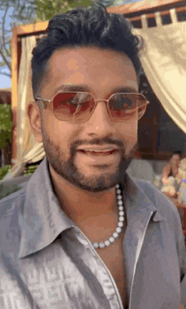 the man is wearing sunglasses and a pearl necklace .
