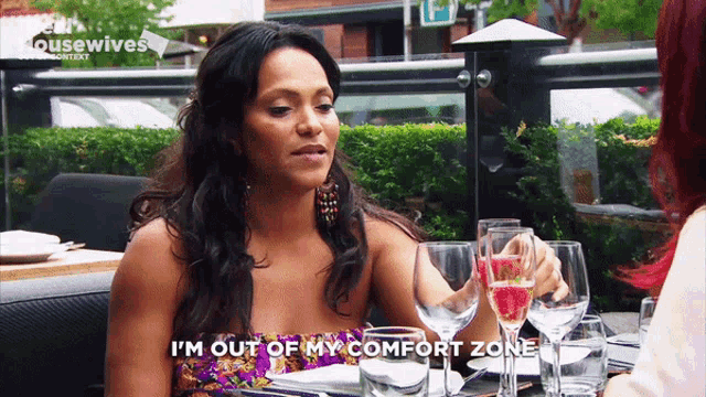 a woman sitting at a table with wine glasses and says i 'm out of my comfort zone