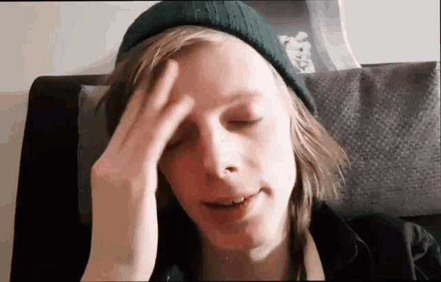 a man wearing a green beanie is holding his head