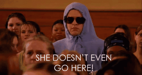 a woman in a hoodie and sunglasses stands in a crowd with the words she doesn 't even go here