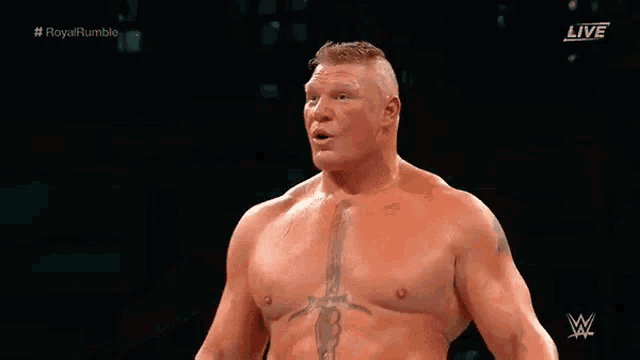 a shirtless wrestler is standing in a ring with his arms outstretched and a tattoo on his chest .