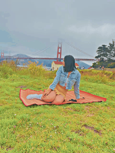 a woman sits on a blanket in front of a bridge