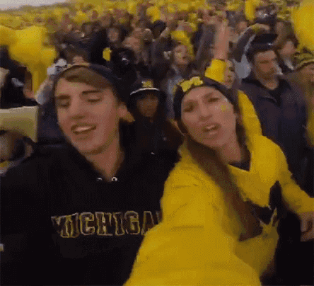 a man and a woman wearing michigan sweatshirts are dancing in a crowd .