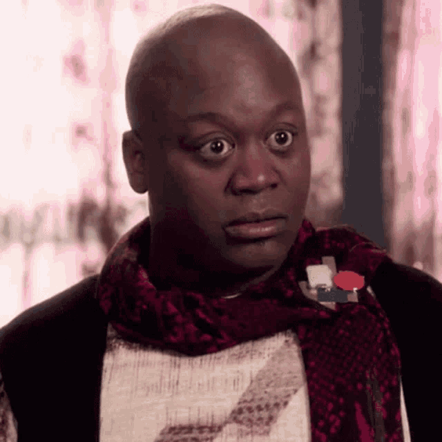 a bald man wearing a scarf and a snake print shirt looks surprised