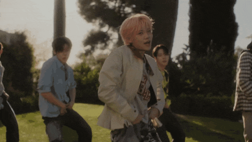 a group of young men are dancing in a park and one of them is wearing a white jacket with the letter r on the front
