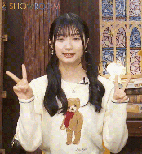 a girl wearing a white sweater with a teddy bear on it giving the peace sign