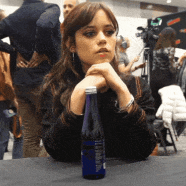a woman sits at a table with a bottle of water with a blue label