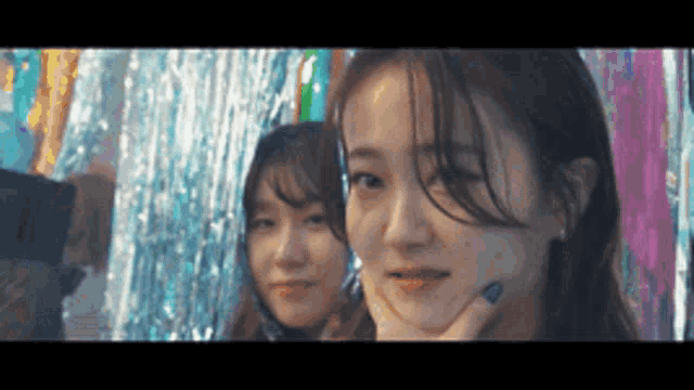 two girls are posing for a picture in front of a colorful backdrop .