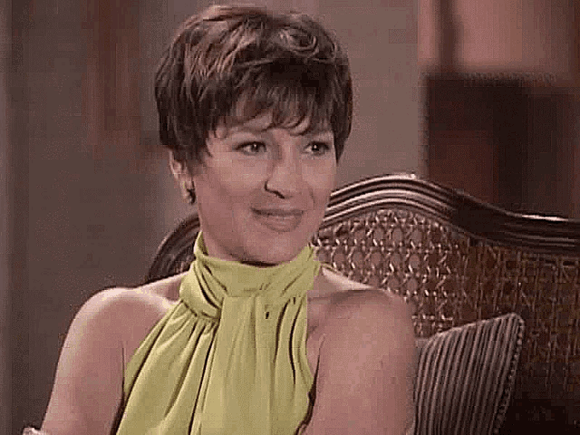 a woman is sitting on a couch wearing a green top and smiling .
