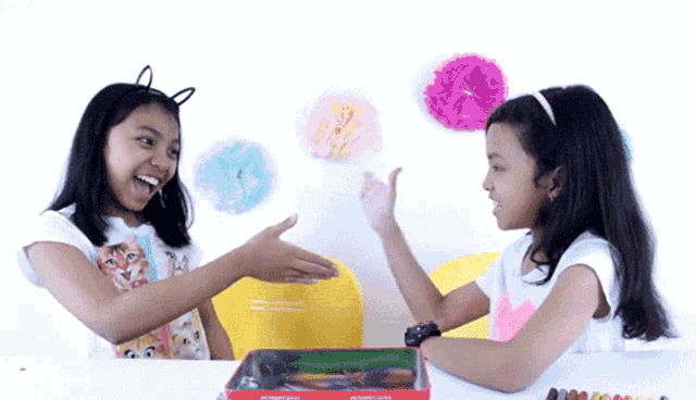 two girls are sitting at a table shaking hands