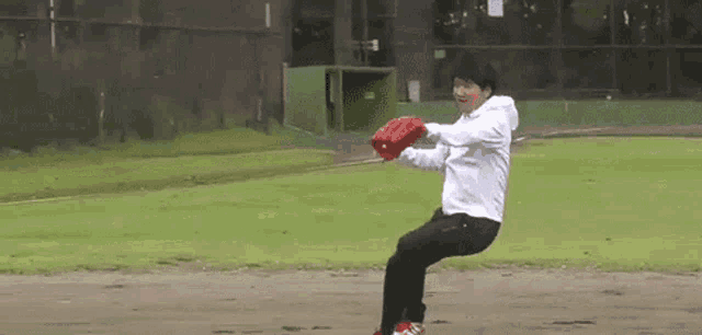 a man in a white jacket is catching a baseball with a red mitt .