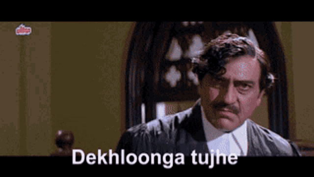 a man with a mustache is standing in front of a sign that says dekhloonga tujh