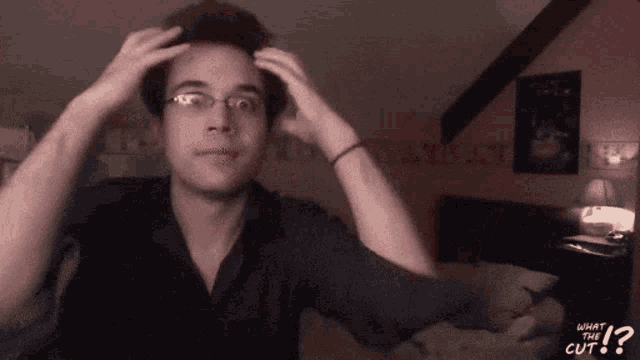 a man with glasses scratches his head with the words what the cut on the bottom