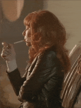 a woman with red hair is smoking a cigarette while wearing a leather jacket