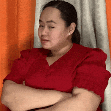 a woman in a red shirt with her arms crossed looks at the camera